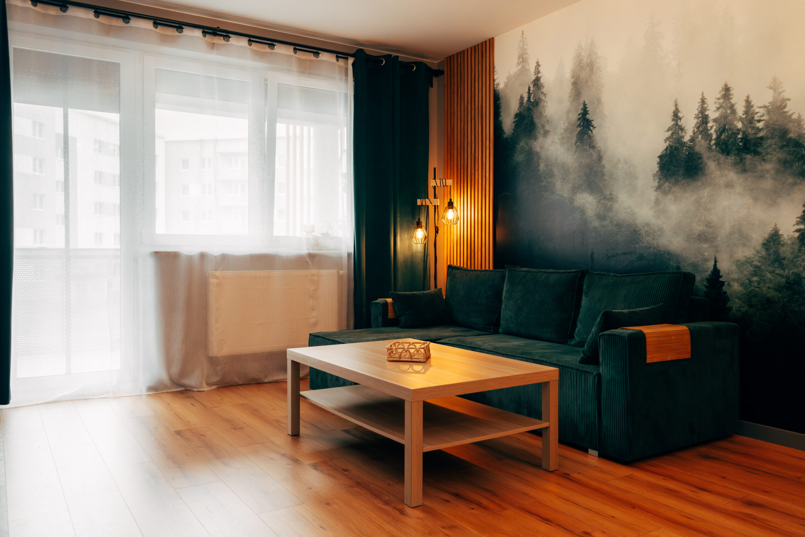 Stylowy salon z zieloną kanapą, fototapetą lasu we mgle i dekoracyjnymi lamelami. Fotografia wnętrz Gorzów Wielkopolski, Wawrów.
