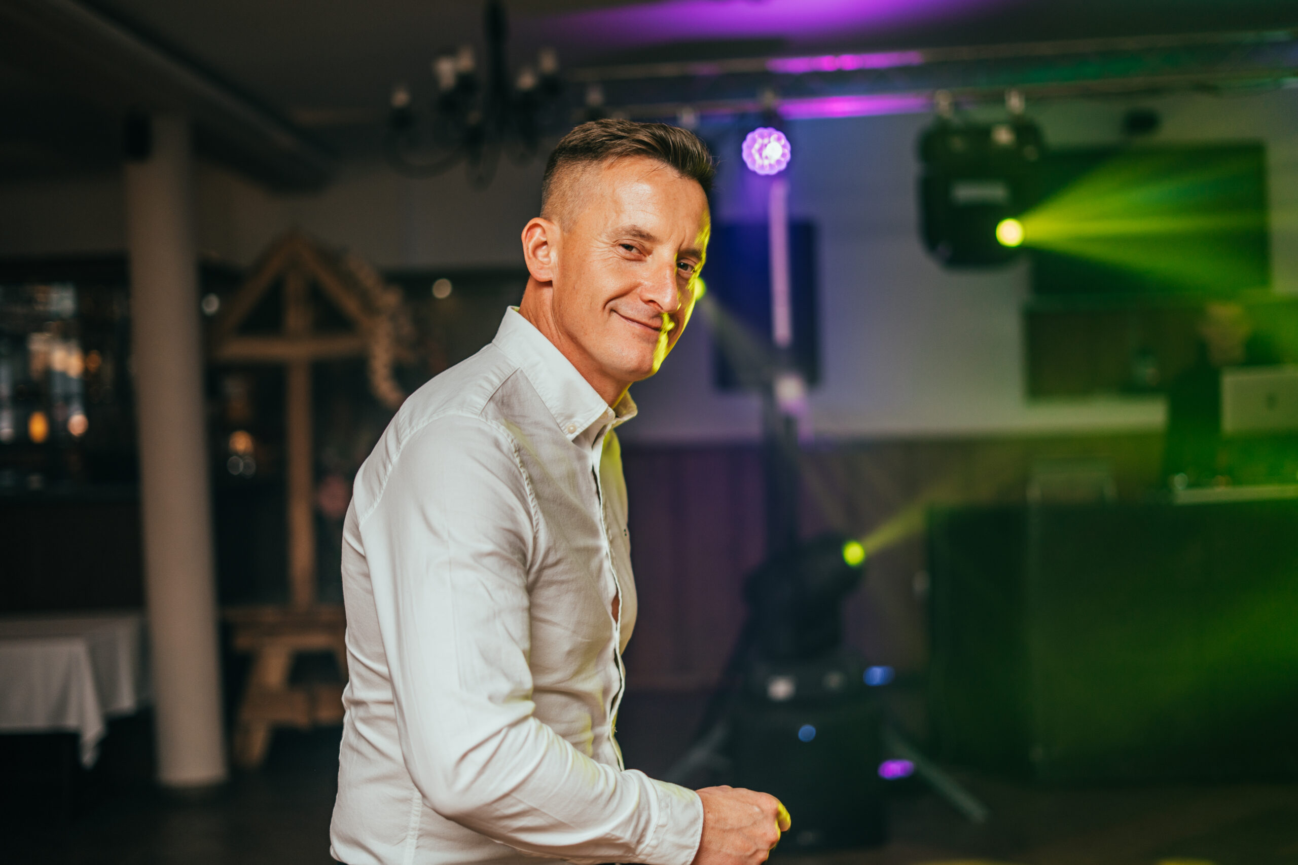 Gość urodzinowy tańczący na parkiecie, patrzący w obiektyw, kolorowe światła DJ-a w tle. Fotografia eventowa Gorzów Wielkopolski, Strzelce Krajeńskie.