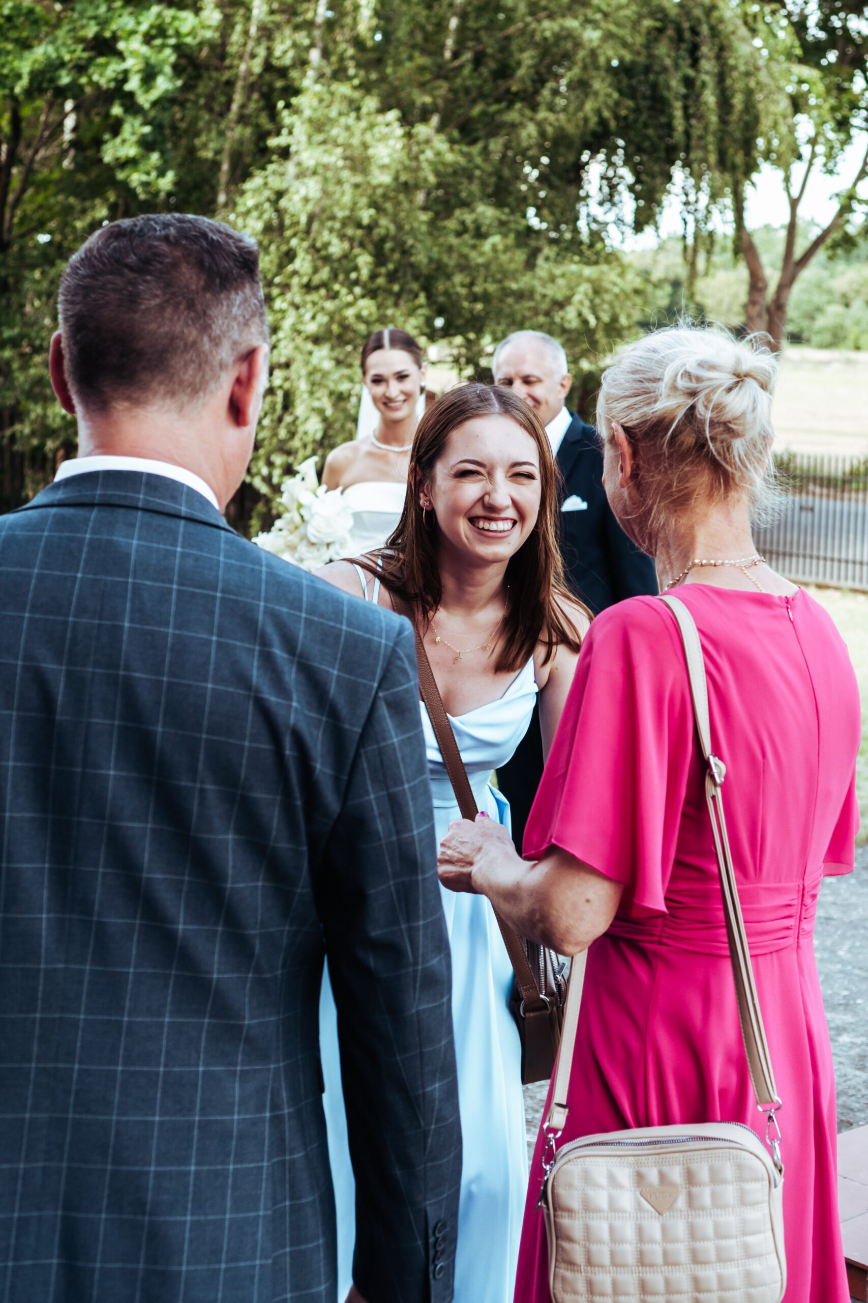 Goście weselni zgromadzeni przed kościołem, w tle Panna Młoda z ojcem. Fotografia ślubna reportażowa Strzelce Krajeńskie, Nowe Kurowo.
