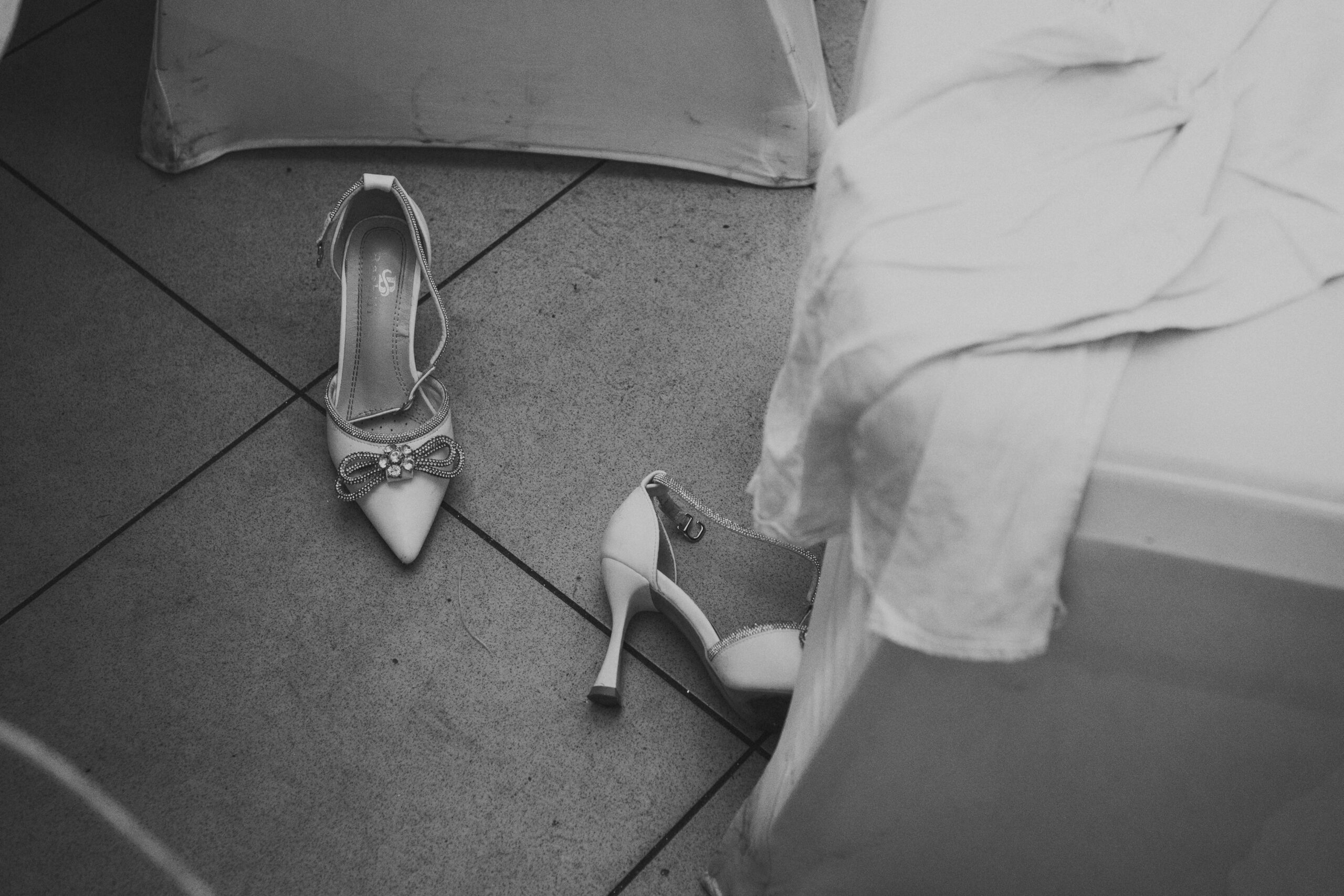 Artystyczne czarno-białe zdjęcie przewróconych butów panny młodej przy stole weselnym. Fotografia ślubna Gorzów Wielkopolski, Słubice.