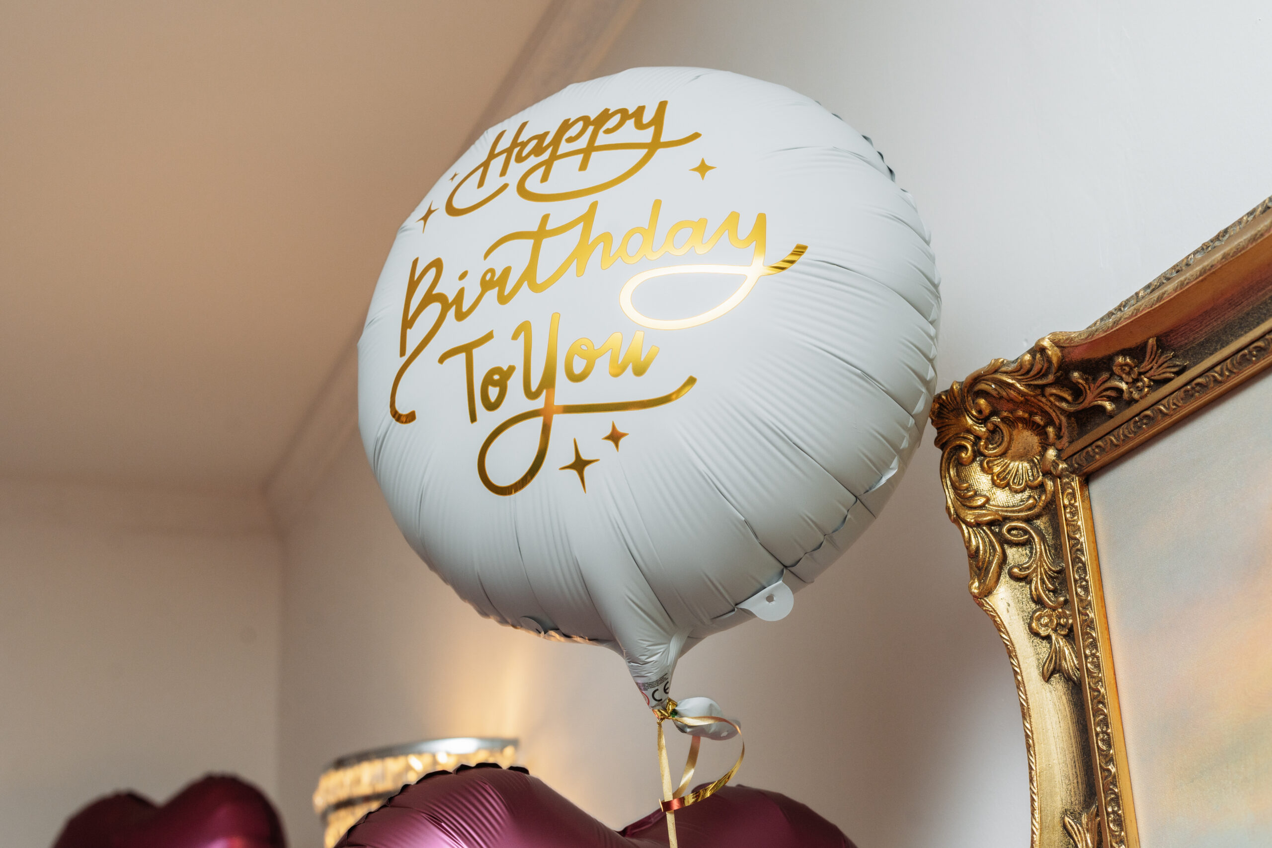 Biały balon z eleganckim złotym napisem Happy Birthday to You na tle dekoracji przyjęcia.