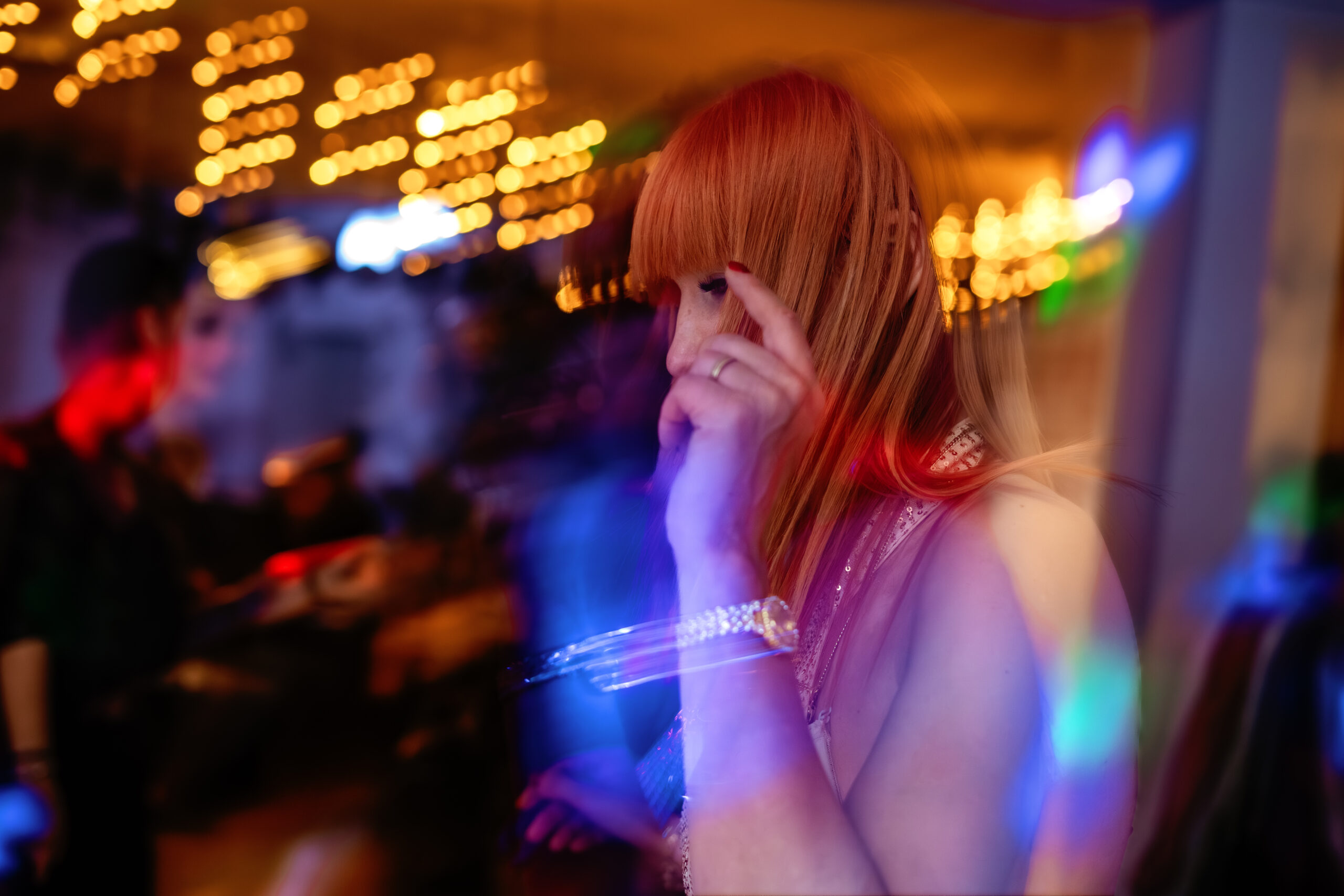Artystyczny portret jubilatki widocznej za rozmytymi, kolorowymi punktami świetlnymi tworzącymi efekt bokeh.