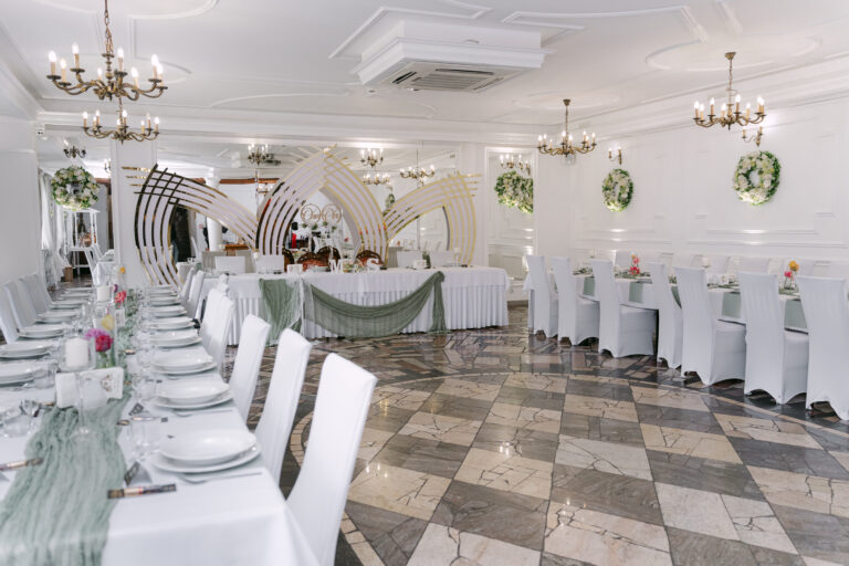 Przestronna, klasyczna sala weselna w Dworku Kurowskim z widokiem na stół prezydialny pary młodej. Eleganckie dekoracje ze szałwiowymi akcentami, nowoczesna geometryczna ścianka ślubna i żyrandole.