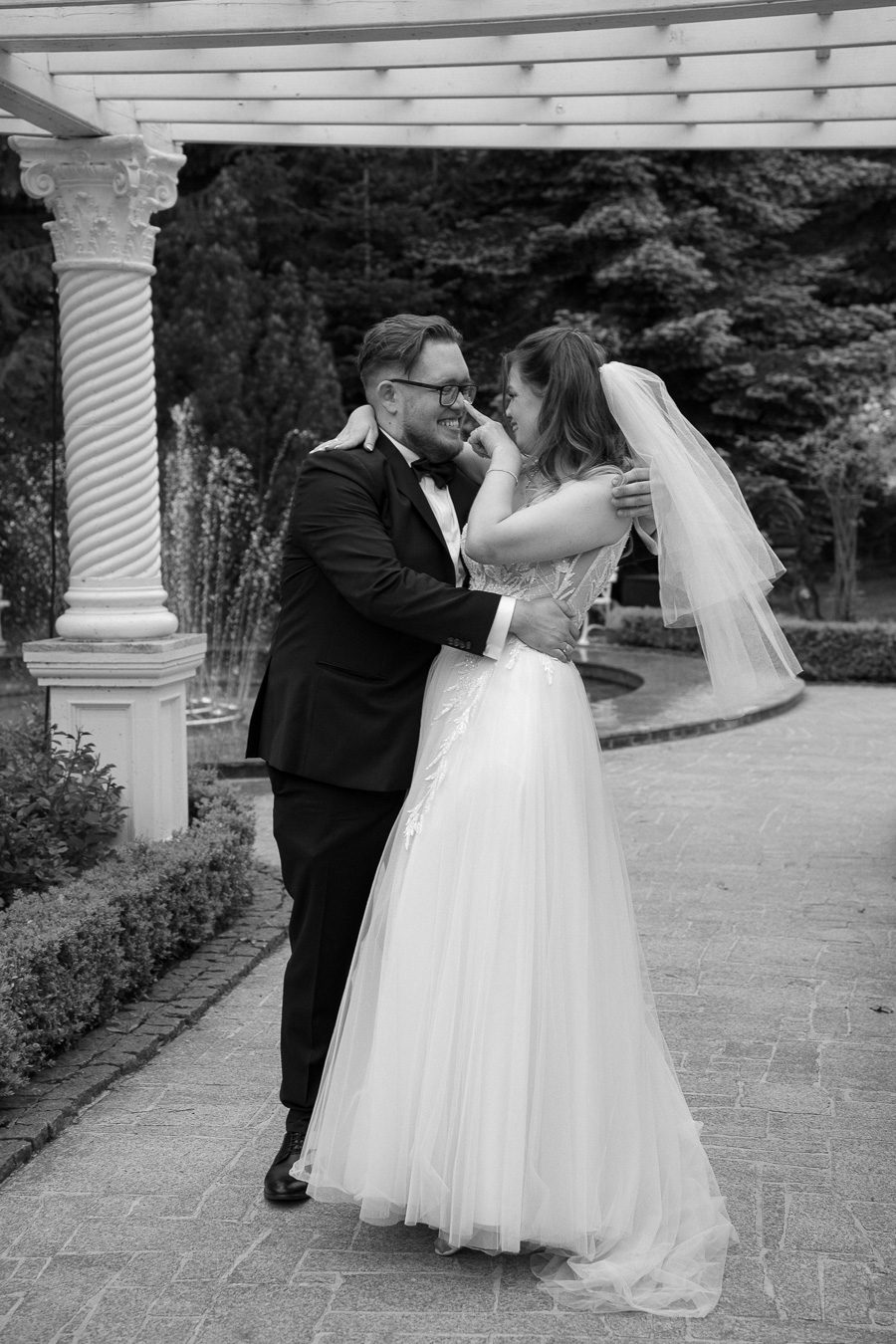 Panna młoda dotyka palcem nosa pana młodego podczas czułego uścisku, romantyczny i czarno-biały reportaż ślubny.