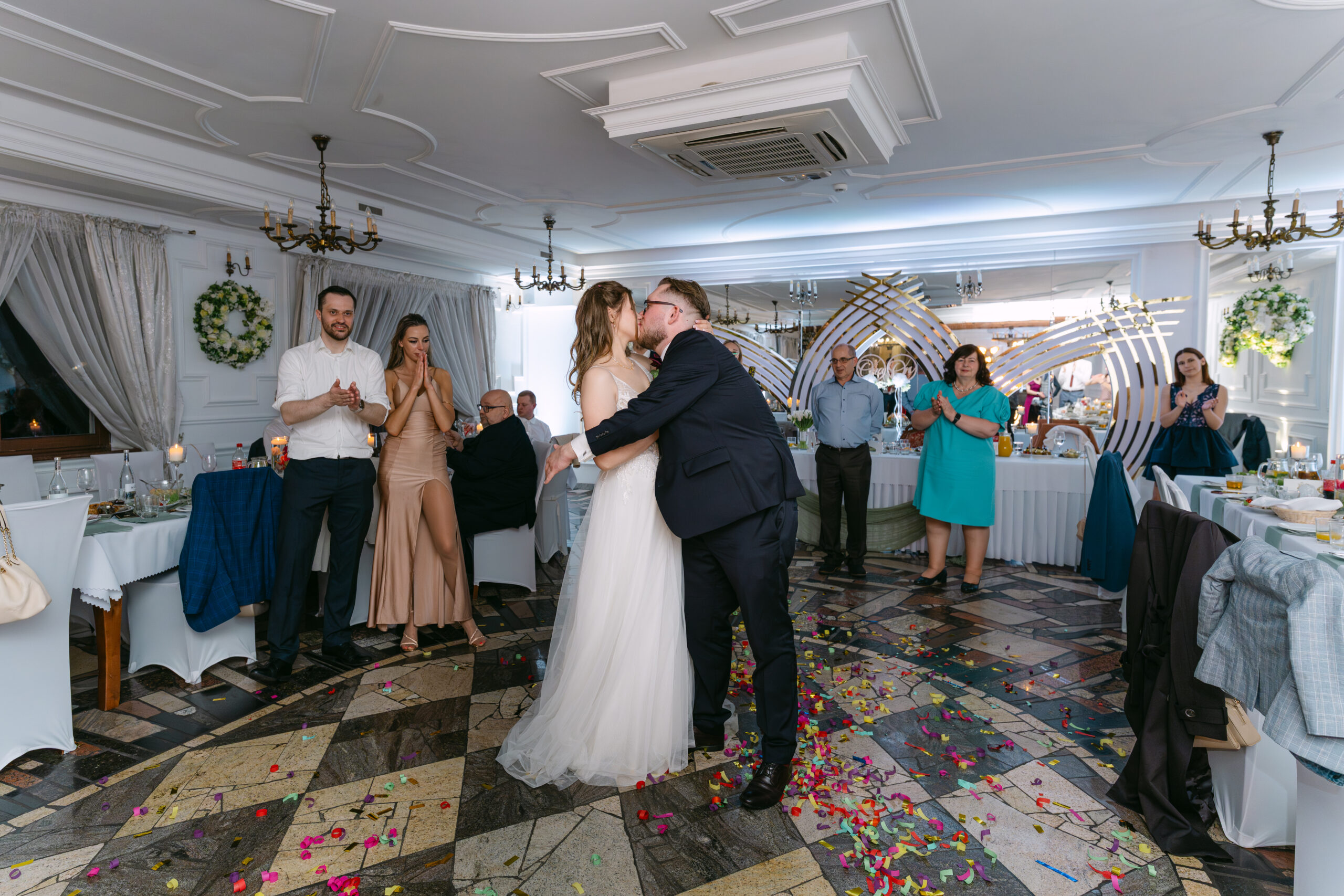 Nowożeńcy Monika i Sebastian całujący się na sali weselnej w otoczeniu klaszczących gości. Romantyczny moment uchwycony w reportażu ślubnym z Dworku Kurowskiego.
